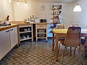 Une cuisine compacte avec un coin repas, dotée d’un sol à motifs, de meubles en bois et d’une horloge au mur.