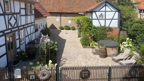 A traditional half-timbered building with a tiled roof, a garden with potted plants and a wooden barrel, and a sign indicating a restaurant.