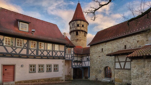 A historic town square with traditional half-timbered buildings, a stone tower, and cobblestone streets.