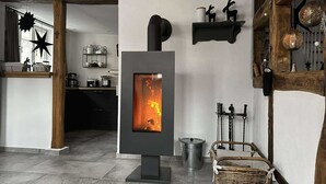 A modern kitchen with a central wood-burning stove, a dining area, and a cozy seating space with a wicker basket.