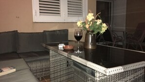 A dining area with a glass-top table, wicker chairs, a vase with flowers, and a wine glass. - quiet apartment with a dream terracce, swimming pool, near the beach (Porís)
