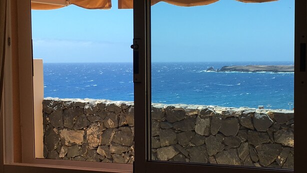 A stone wall and a view of the ocean through a window with a curtain. - quiet apartment with a dream terracce, swimming pool, near the beach (Porís)