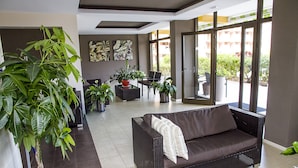 A modern living room with a dark brown sofa, a large potted plant, and a dining area with a laptop. - 150 m from the sandy beach, fantastic sunsets, WiFi, satellite TV, swimming pools (Costa Adeje)