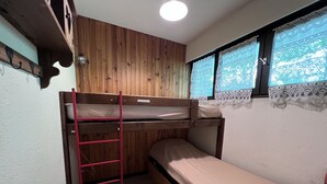 A bunk bed room with wooden walls, a window with lace curtains, and a wooden shelf above the bed. - CRYSTAL 14 - Village center apartment, close to the slopes, mountain view - Garage (La Clusaz)