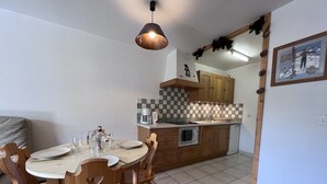 A dining area with a round table, wooden chairs, and a hanging pendant light. - CRYSTAL 14 - Village center apartment, close to the slopes, mountain view - Garage (La Clusaz)