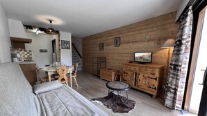 A cozy living room with a sofa, a dining table with chairs, a kitchen area, and a TV on a wooden cabinet. - CRYSTAL 14 - Village center apartment, close to the slopes, mountain view - Garage (La Clusaz)