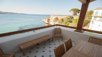 Un balcon avec une table et des chaises en bois, un banc et une vue sur la mer et la côte.