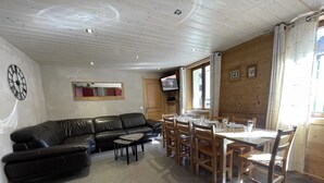 A cozy living room with a black leather sofa, a small coffee table, and a dining area with wooden chairs and a table set for four. - GENTIANES 1 – Lovely apartment in the village center and close to the slopes – Wi-Fi (La Clusaz)