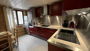A modern kitchen with stainless steel appliances, red cabinetry, and a wooden dining table with chairs. - GENTIANES 1 – Lovely apartment in the village center and close to the slopes – Wi-Fi (La Clusaz)