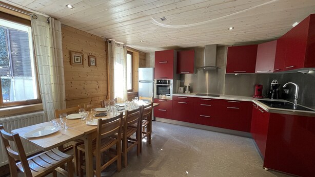 A kitchen with wooden cabinets, a stainless steel refrigerator, and a dining area with a table set for four. - GENTIANES 1 – Lovely apartment in the village center and close to the slopes – Wi-Fi (La Clusaz)