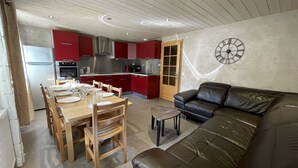 A modern kitchen with red cabinets, a dining table set for six, and a black leather sofa in a living area. - GENTIANES 1 – Lovely apartment in the village center and close to the slopes – Wi-Fi (La Clusaz)