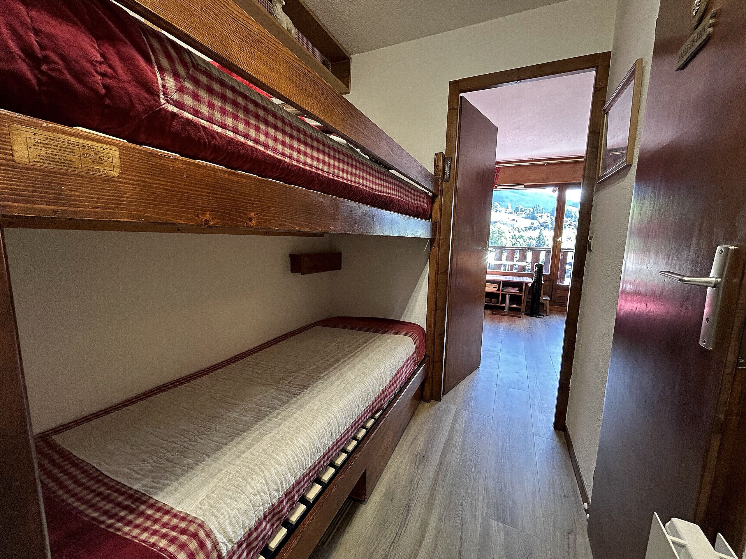 A narrow corridor with bunk beds, wooden flooring, and a door leading to an outdoor area.