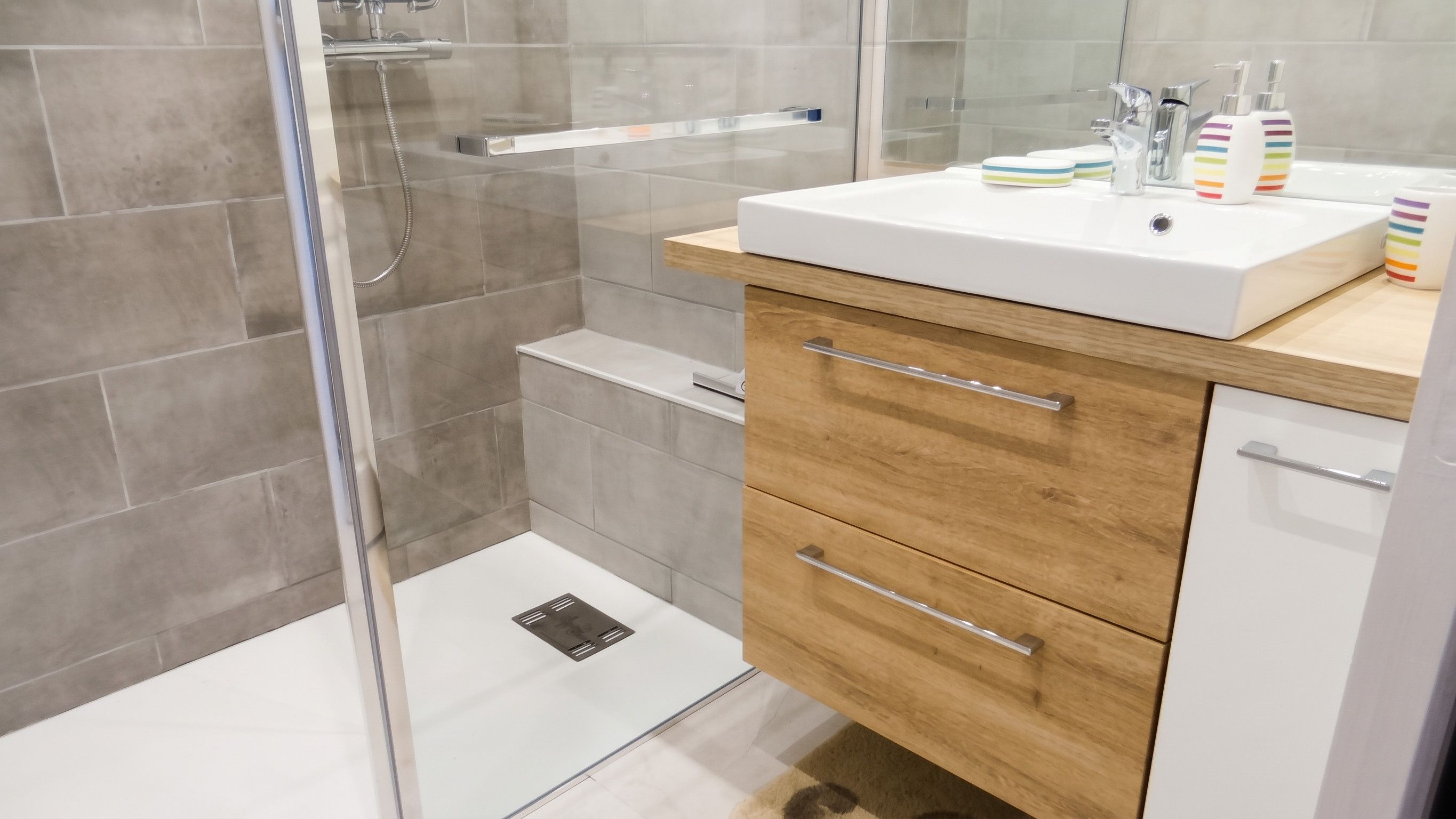 A modern bathroom with a glass shower enclosure, a white sink with a wooden countertop, and a wooden cabinet with drawers.
