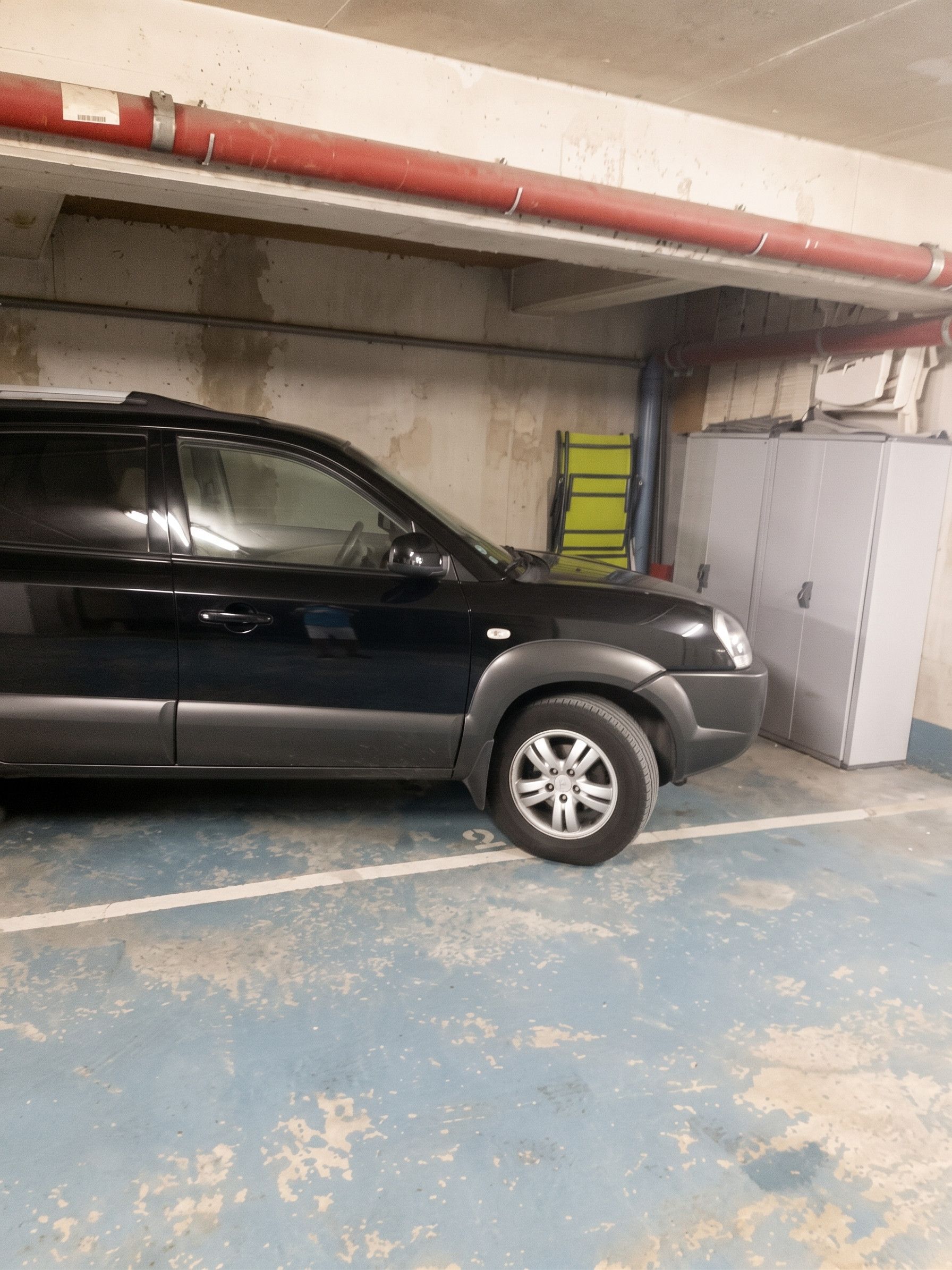 Un SUV negro estacionado en un garaje con piso de concreto y una barrera de seguridad amarilla.