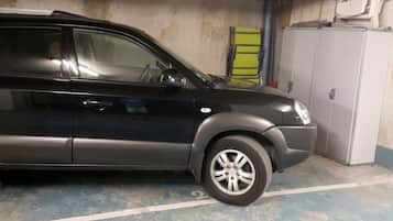 Un SUV negro estacionado en un garaje con piso de concreto y una barrera de seguridad amarilla.