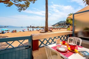 A balcony with a table set for dining, overlooking a beach with people and boats. - Homerez - Apartment in Théoule-sur-Mer. (Théoule-sur-Mer)