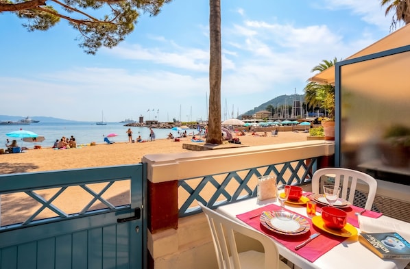 A balcony with a table set for dining, overlooking a beach with people and boats.