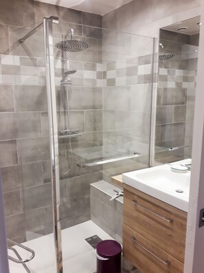 A modern bathroom with a glass-enclosed shower, a white sink with a wooden vanity, and a mirror.
