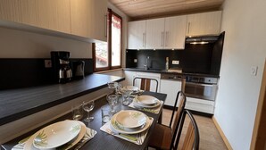 Uma cozinha moderna com armários de madeira, bancada preta e um espaço de jantar para quatro pessoas, com pratos, copos e talheres.