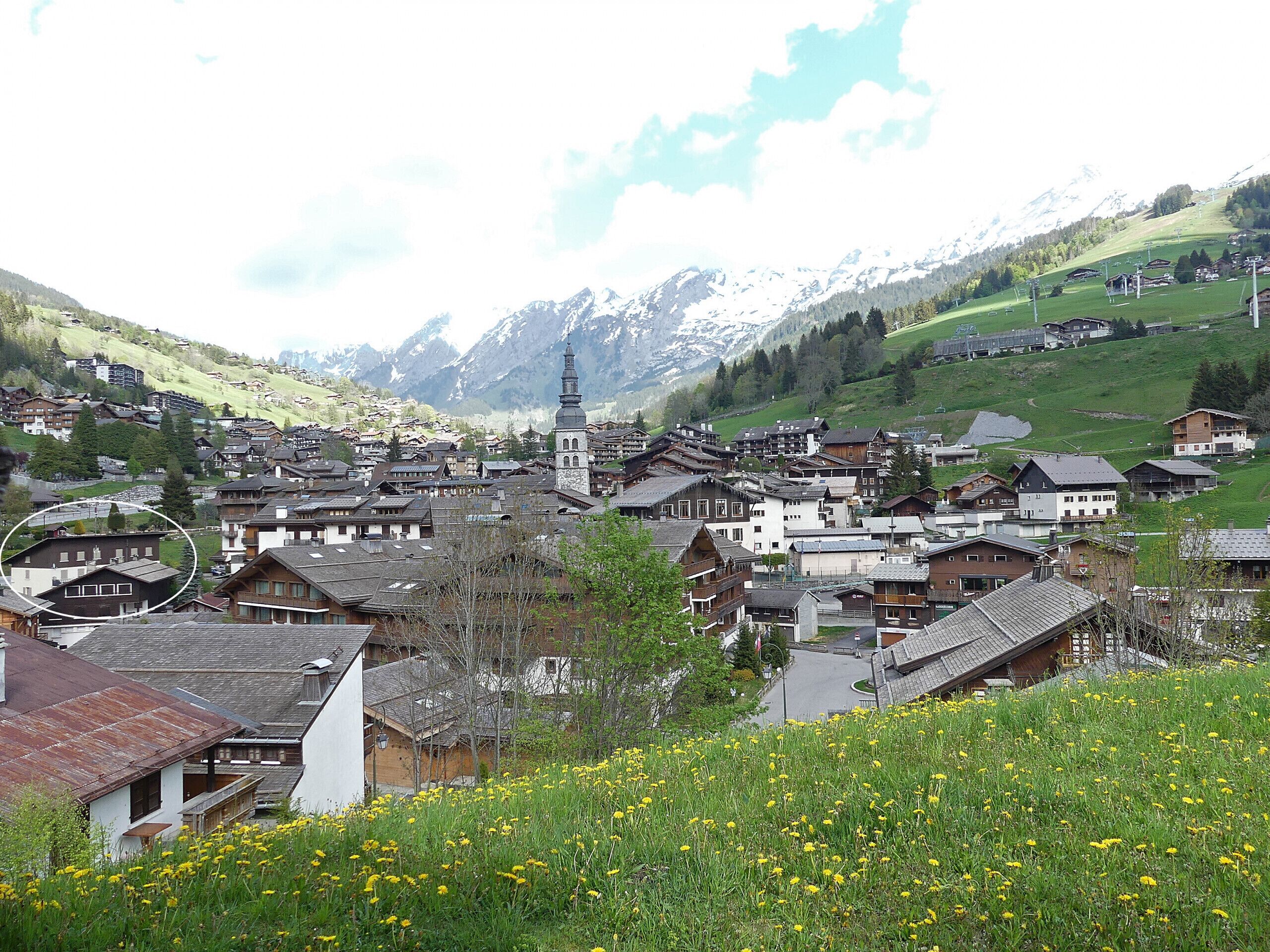 A mountainous village with traditional wooden houses, a church, and a clear view of snow-capped peaks in the background.