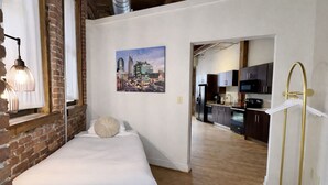 Une chambre à coucher avec un lit, un oreiller, un luminaire suspendu et un tableau représentant un paysage urbain accroché au mur.