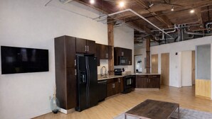 Une cuisine moderne avec des meubles en bois foncé, des appareils électroménagers en acier inoxydable et un grand téléviseur à écran plat fixé au mur.