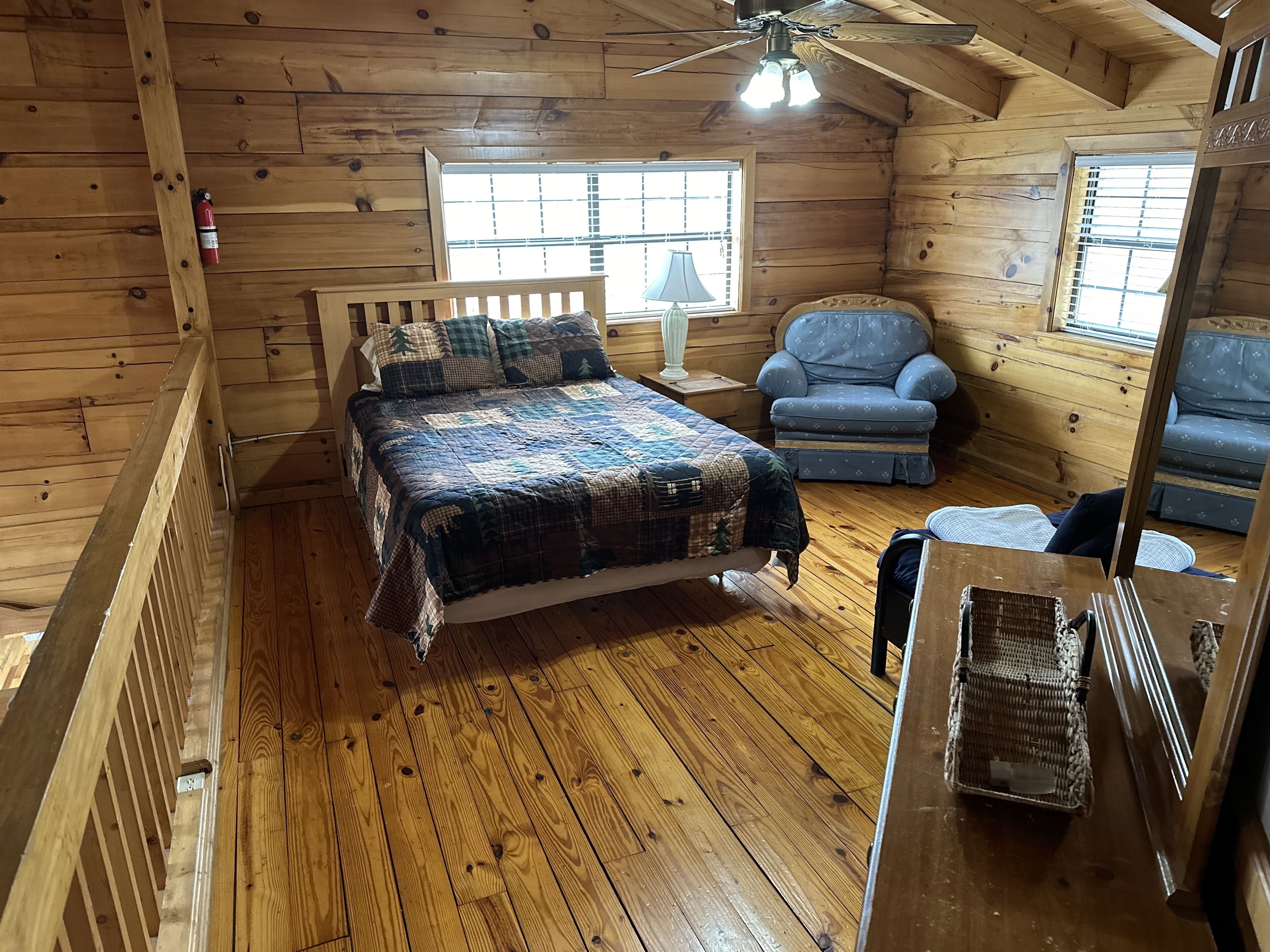 Une chambre confortable dans un chalet, avec un plancher en bois, un lit recouvert d’une couverture à carreaux, un fauteuil bleu et une petite table.
