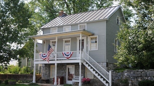 A two-story house with a porch, stone foundation, and a flag.