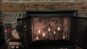 A fireplace with multiple candles, a decorative Santa figurine, and a stone wall backdrop.