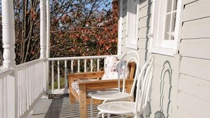 A wooden bench and two white chairs on a porch with a white railing.