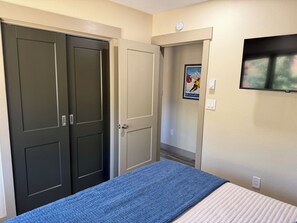A bedroom with a bed, a wardrobe, a poster on the wall, and a television mounted on the wall.