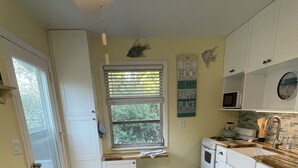 Una cocina con gabinetes blancos, estufa, microondas y ventana con persianas.