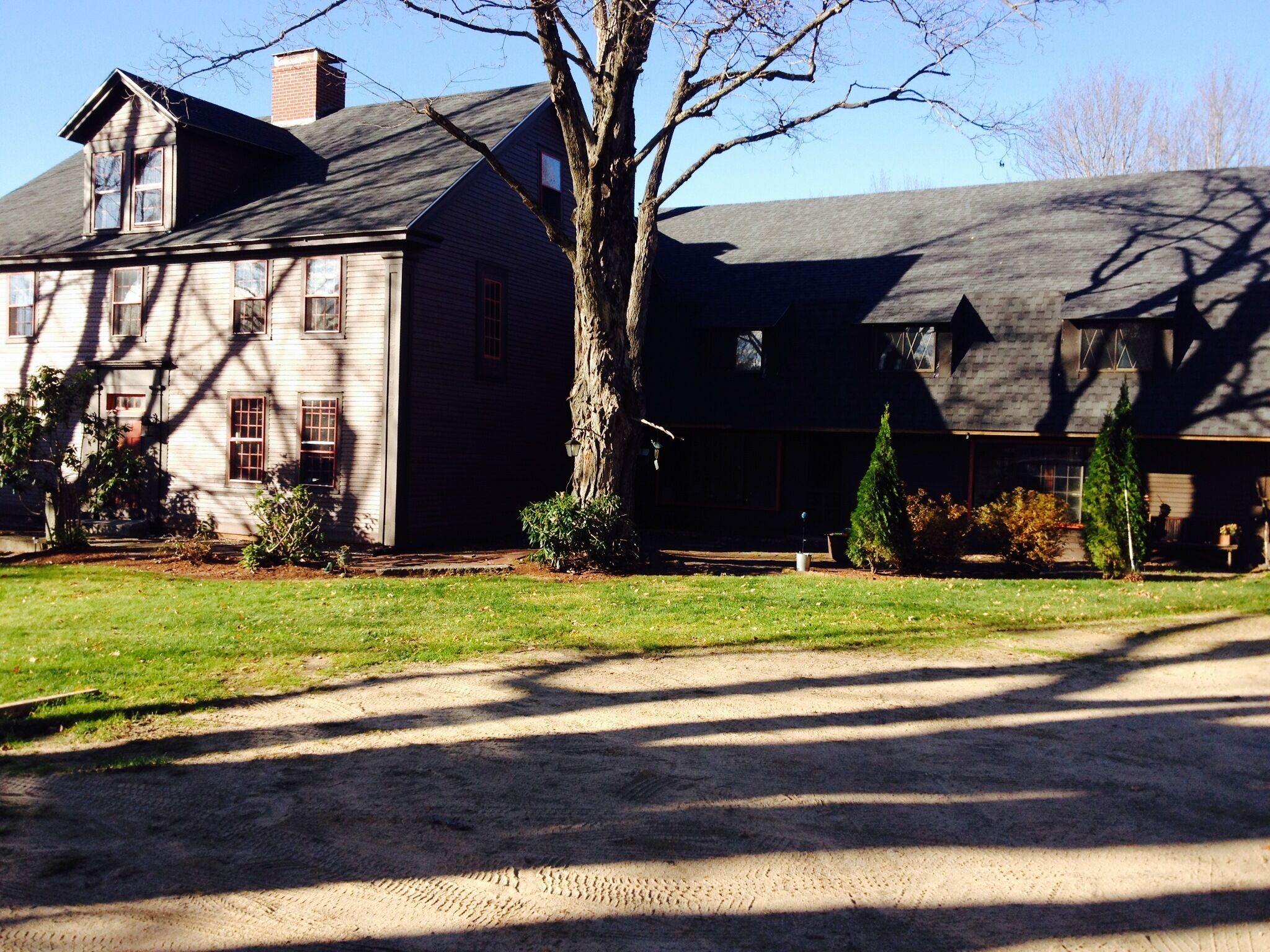 A large, two-story house with a prominent chimney, a well-maintained lawn, and a dirt driveway.