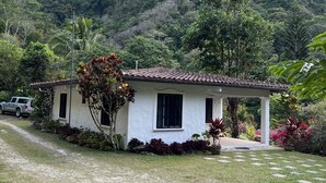 Une maison blanche avec un toit recouvert de tuiles, entourée d’un jardin bien entretenu et d’une allée gravillonnée.