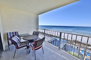 A balcony with a view of the ocean, featuring striped chairs and a round table.