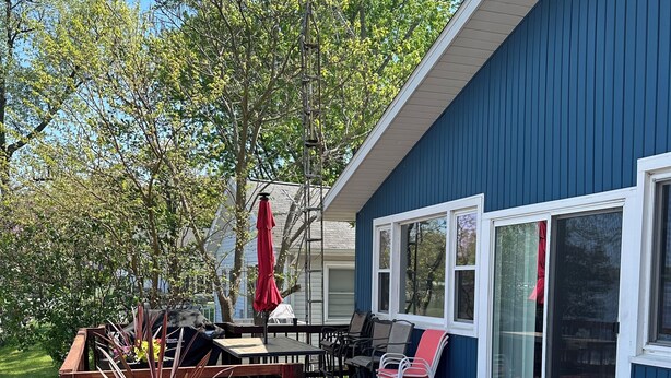 Une terrasse avec une table et des chaises, un jardinier avec des plantes, et un bâtiment bleu doté de grandes fenêtres.