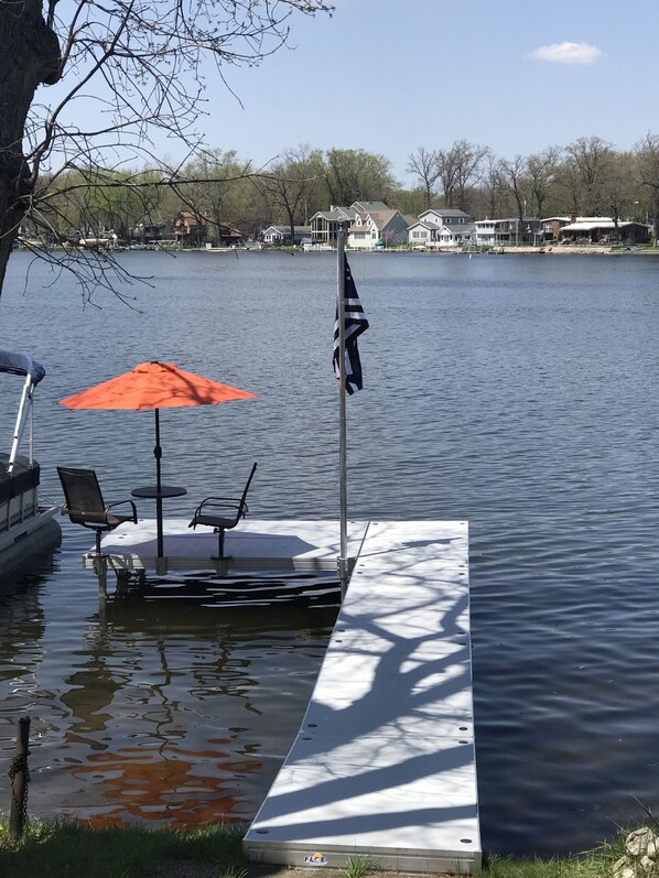 A dock with a flag, a table with chairs, and an umbrella. - Cozy Koontz lake House right on the water, 30 min to Notre Dame <br> (koontz lake)