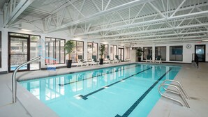En indendørs swimmingpool med tydelige baner, liggestole og et hvælvet loft med metalbjælker.