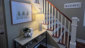 A staircase with a wooden handrail, a console table with decorative items, and a wall sign reading 'BEACH HOUSE'. - Beautiful home in Picturesque setting just steps from Lake Michigan! (Fennville)