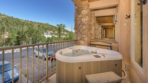Ein Whirlpool auf einem Balkon mit einer Steinwand, Blick auf einen bewaldeten Hang und ein geparktes Auto davor.