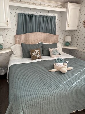Una cama bien hecha con un edredón color turquesa, una almohada decorativa con diseño de estrella y una pequeña cesta de mimbre con un peluche sobre un piso de madera.