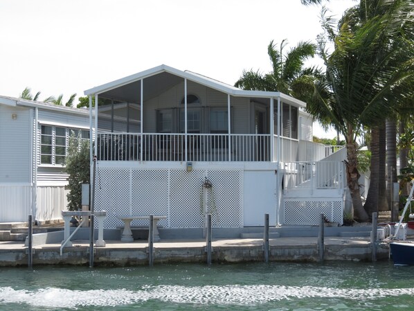 Una casa de dos pisos con balcón, muelle y un bote pequeño.