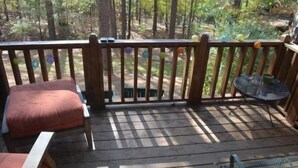 Une terrasse en bois avec une table et des chaises en métal, entourée d’arbres.