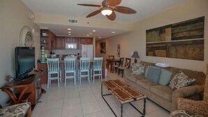 A living room with a sofa, coffee table, and TV. There is a dining area with chairs and a table. A ceiling fan is visible. - 4th Floor! ☼☼❀❀ 2BR/2BA,Sleeps 6,Handicap Acc,Living & Mstr Rms Facing The Beach (Panama City)