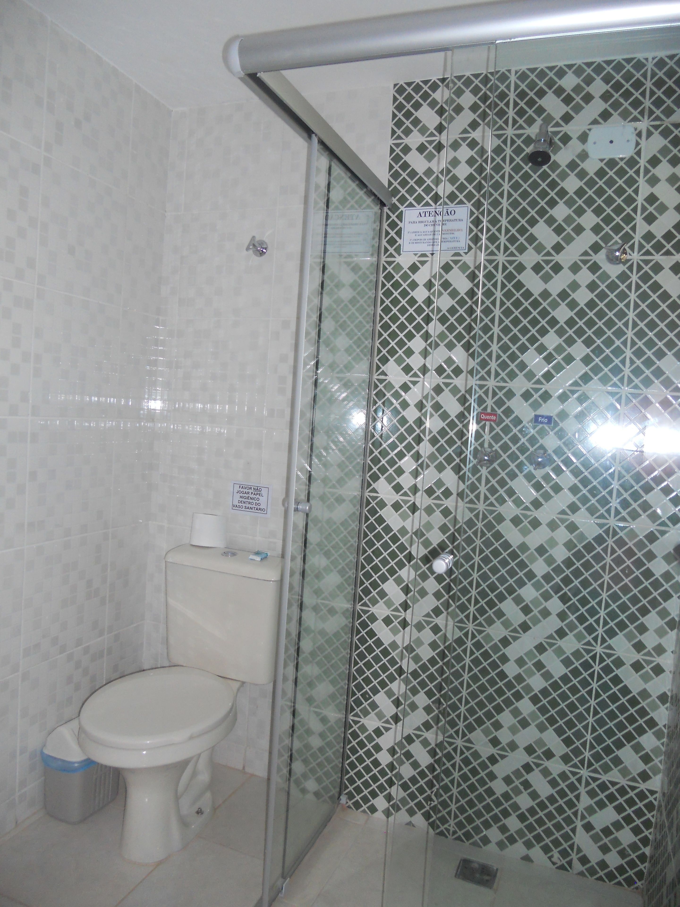 Un baño con inodoro, un cesto de basura y una ducha con pared de azulejos estampados.