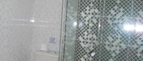A bathroom with a toilet, a trash bin, and a shower with a patterned tile wall.
