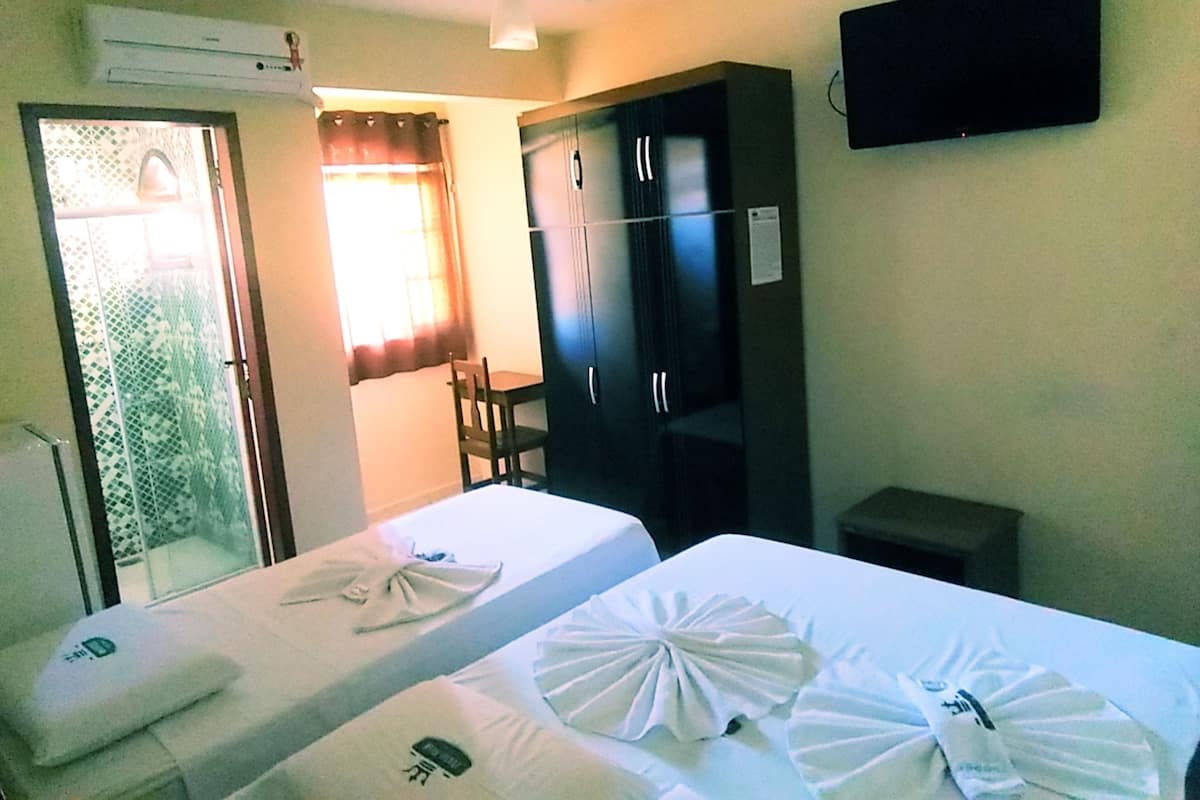 Quarto de hotel com duas camas, um guarda-roupa, uma televisão e um aparelho de ar condicionado.