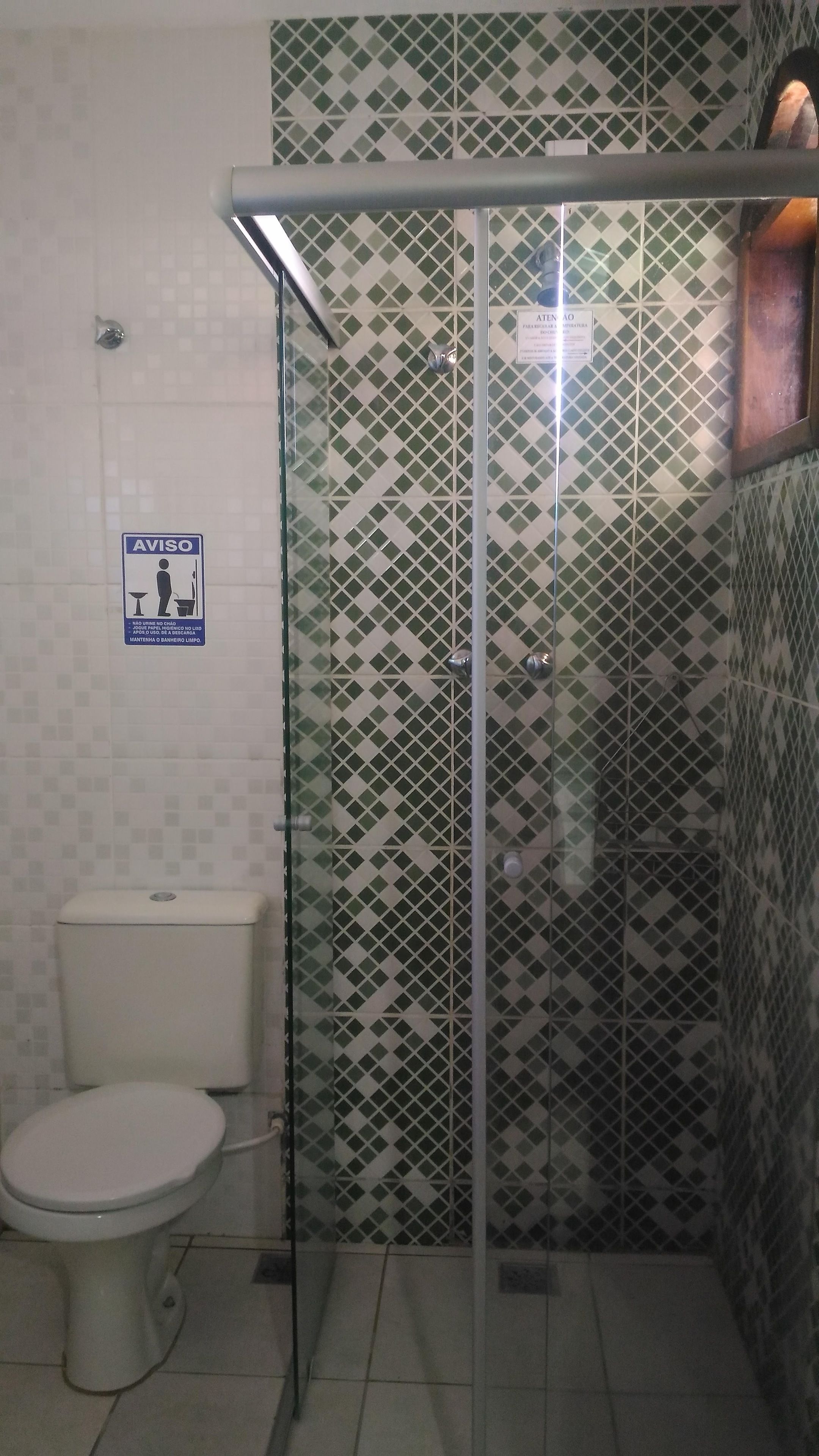 Un baño con inodoro, ducha con puerta de cristal y pared de azulejos estampados.