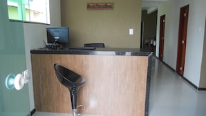 A reception desk with a computer monitor, a wooden counter, and a bar stool. - Hotel Porto Real (Porto Real)