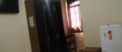 Una camera d'albergo con due letti, una ventola a soffitto, un climatizzatore, una televisione, una scrivania e una sedia.